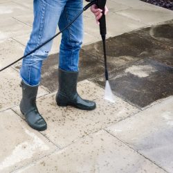 An individual in rubber boots utilizes a pressure washer, effectively removing dirt and grime from a surface.