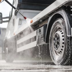 A man uses a pressure washer to clean a truck, showcasing the power of the equipment in action.