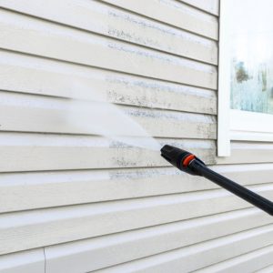 An individual uses a pressure washer to effectively remove dirt from the siding of a residential home.